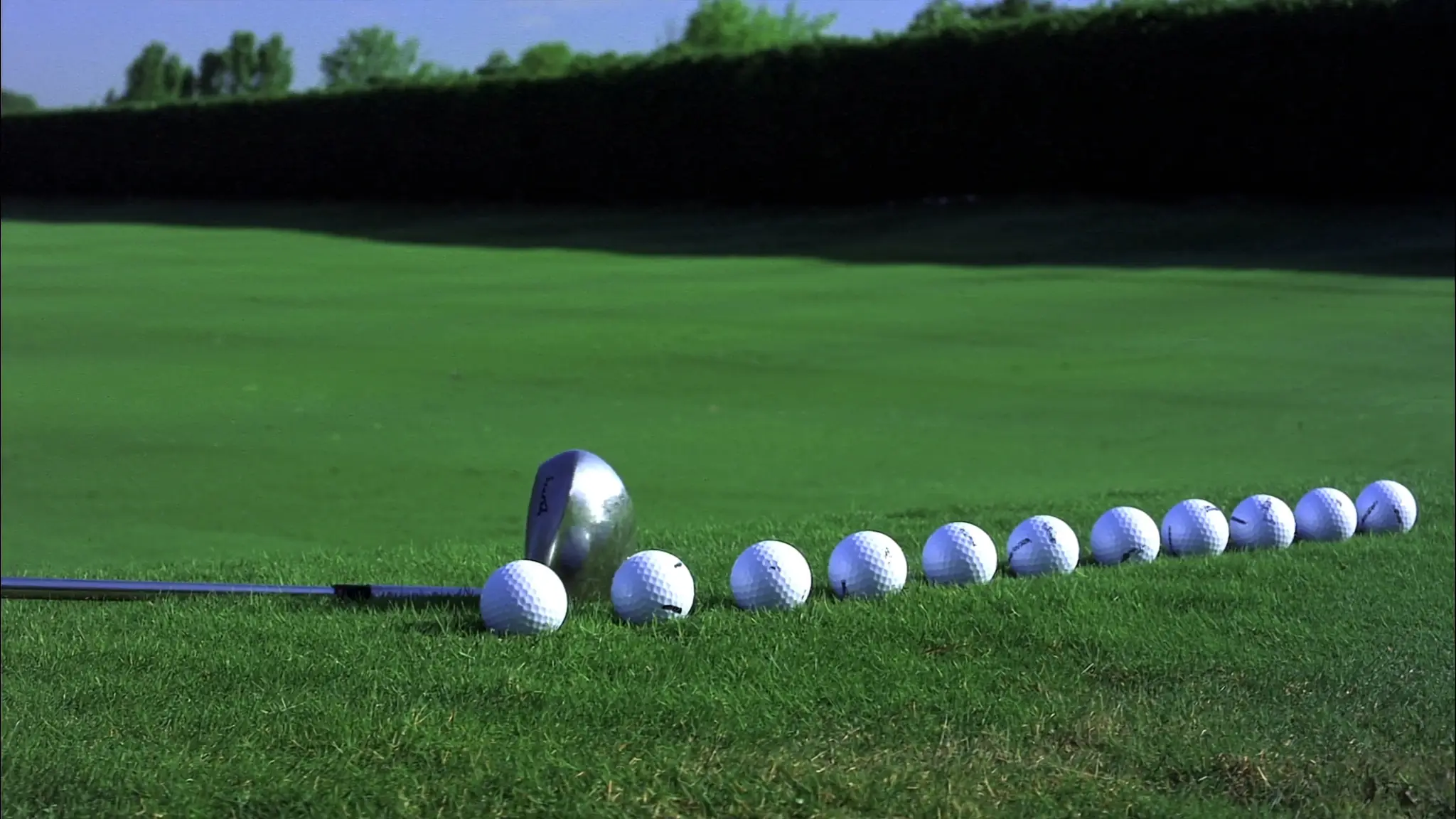 A row of golf balls lined up on the turf of a practice ground beside an iron